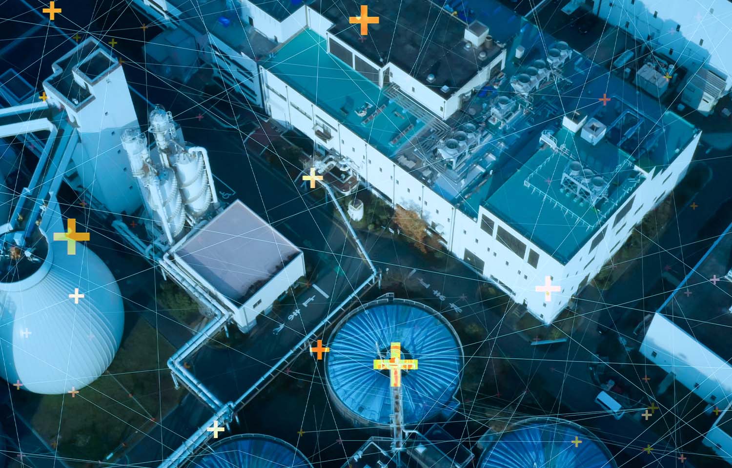 Prédios e construções de uma fábrica vistos de cima, em um tom azulado. Por cima dos prédios e construções, elementos gráficos de linhas e pontos de localização, simulando que todos os elementos estão conectados